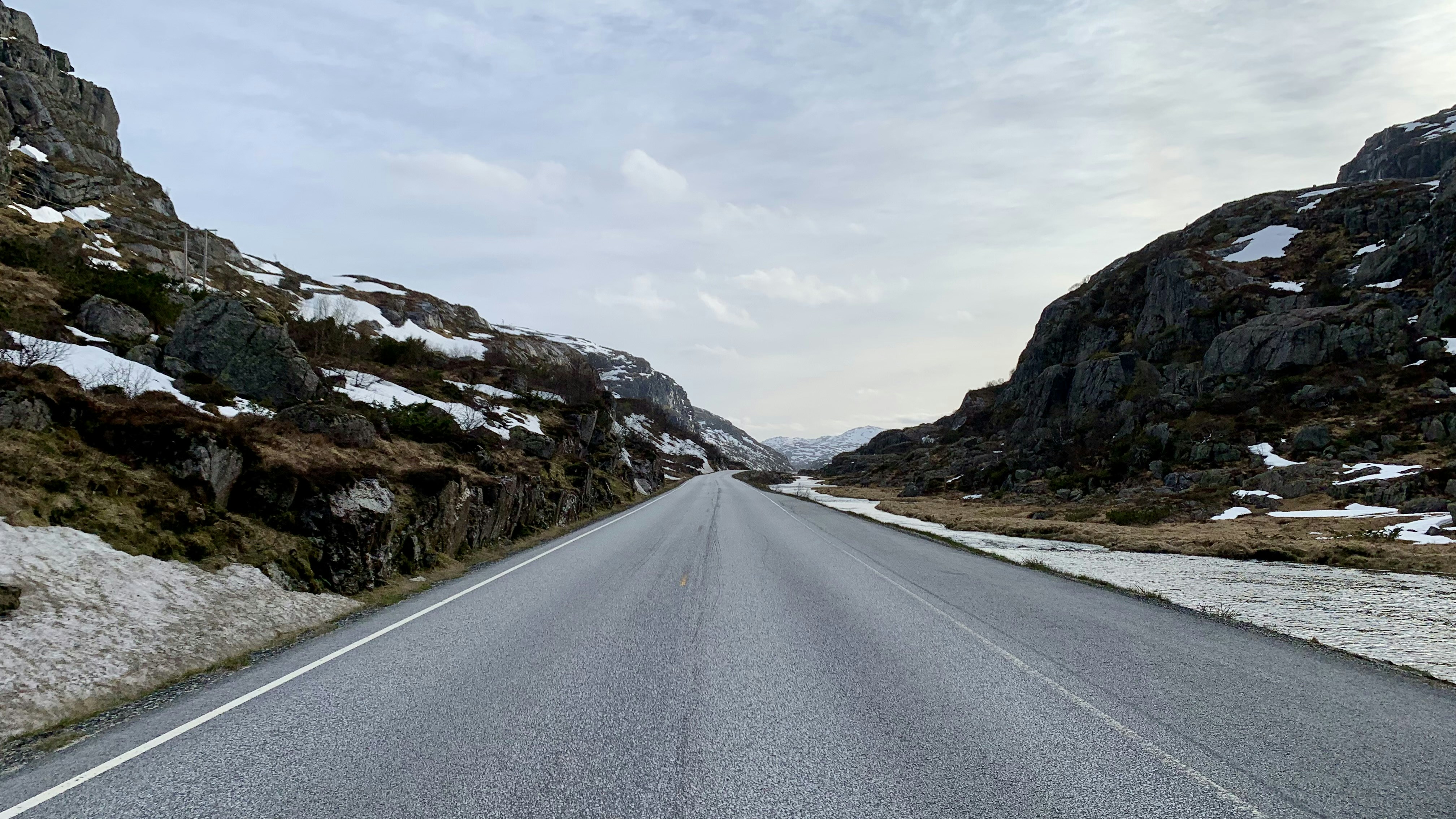 An empty road winds through a snowy mountain pass.