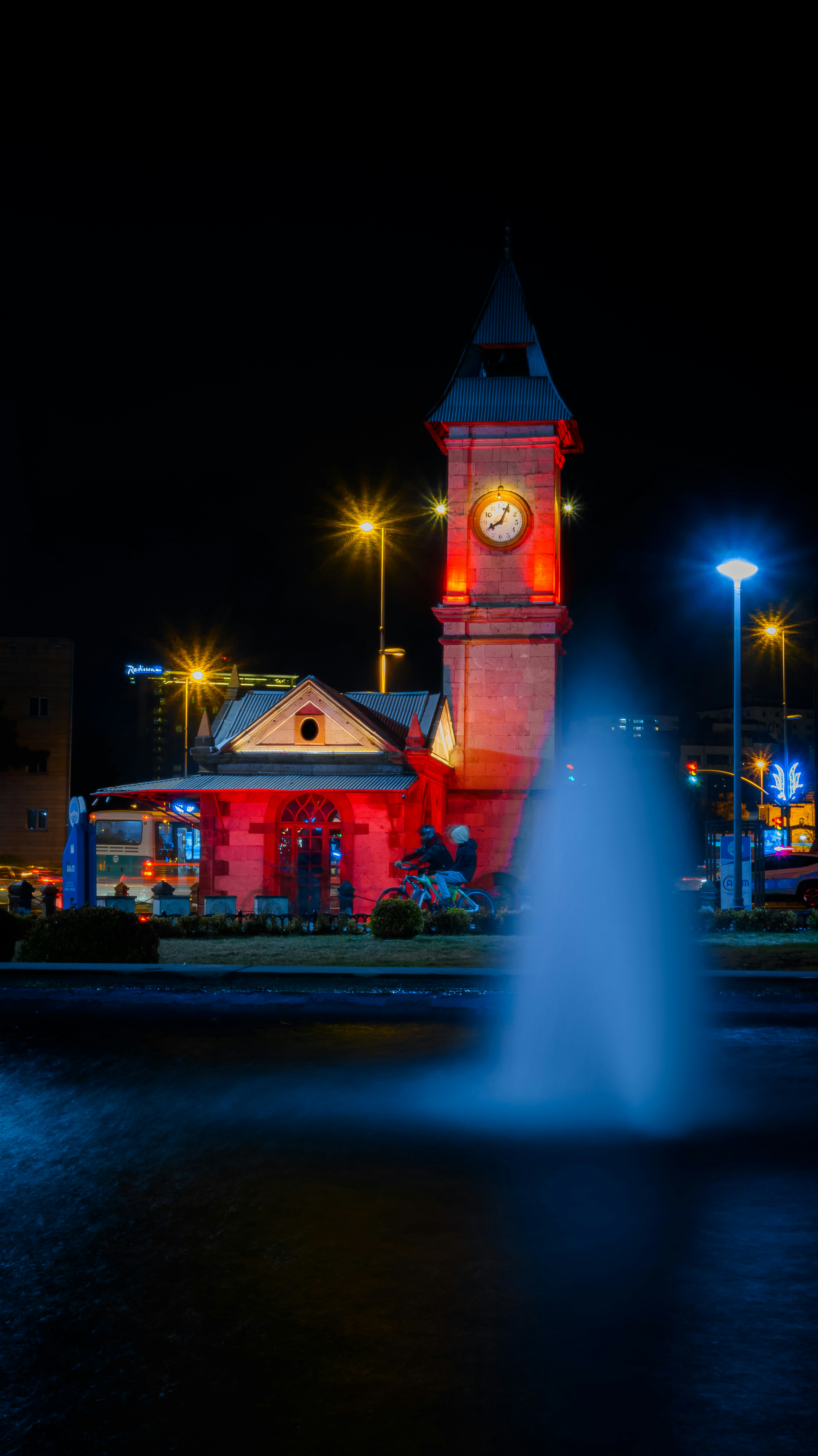 A clock tower and fountain lit up at night.