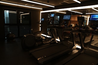 A dimly lit gym with treadmills and monitors