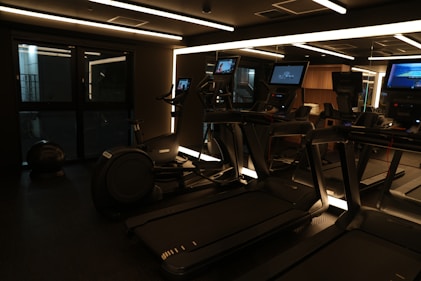 A dimly lit gym with treadmills and monitors