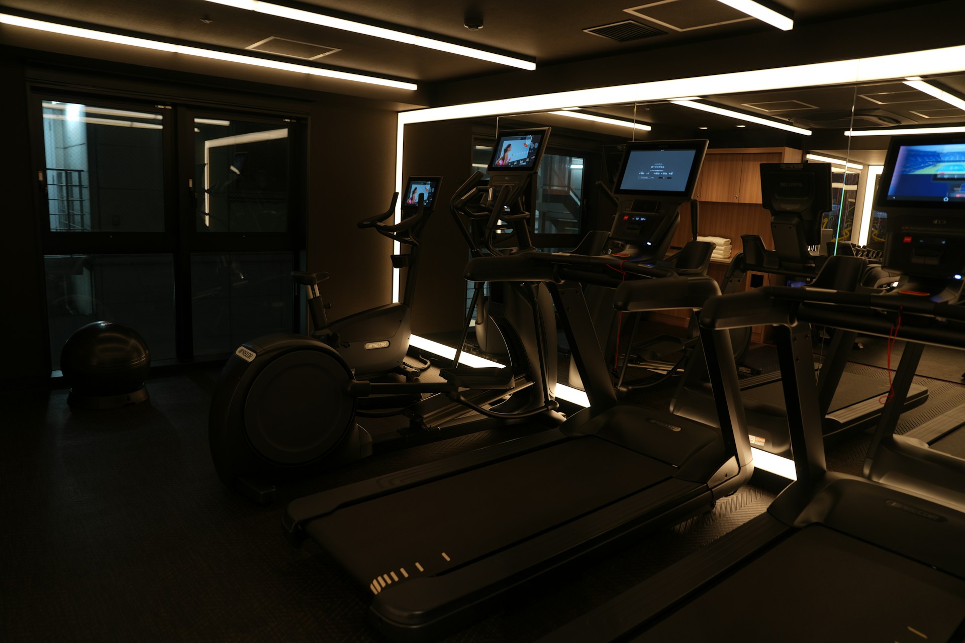 A dimly lit gym with treadmills and monitors