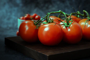 A pile of tomatoes sitting on top of a wooden cutting board