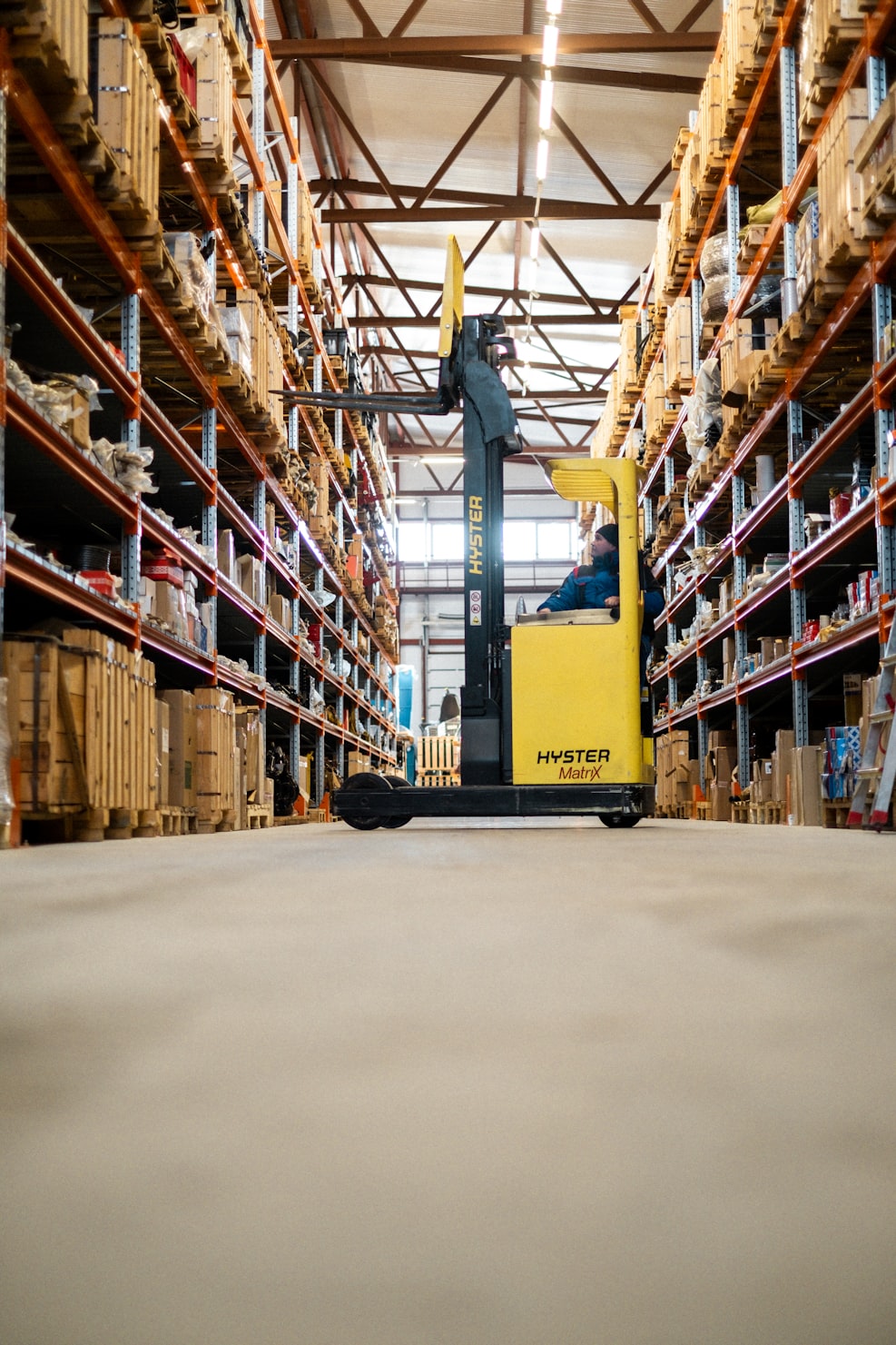 Warehouse aisle with yellow forklift and tall shelving units filled with crates and boxes