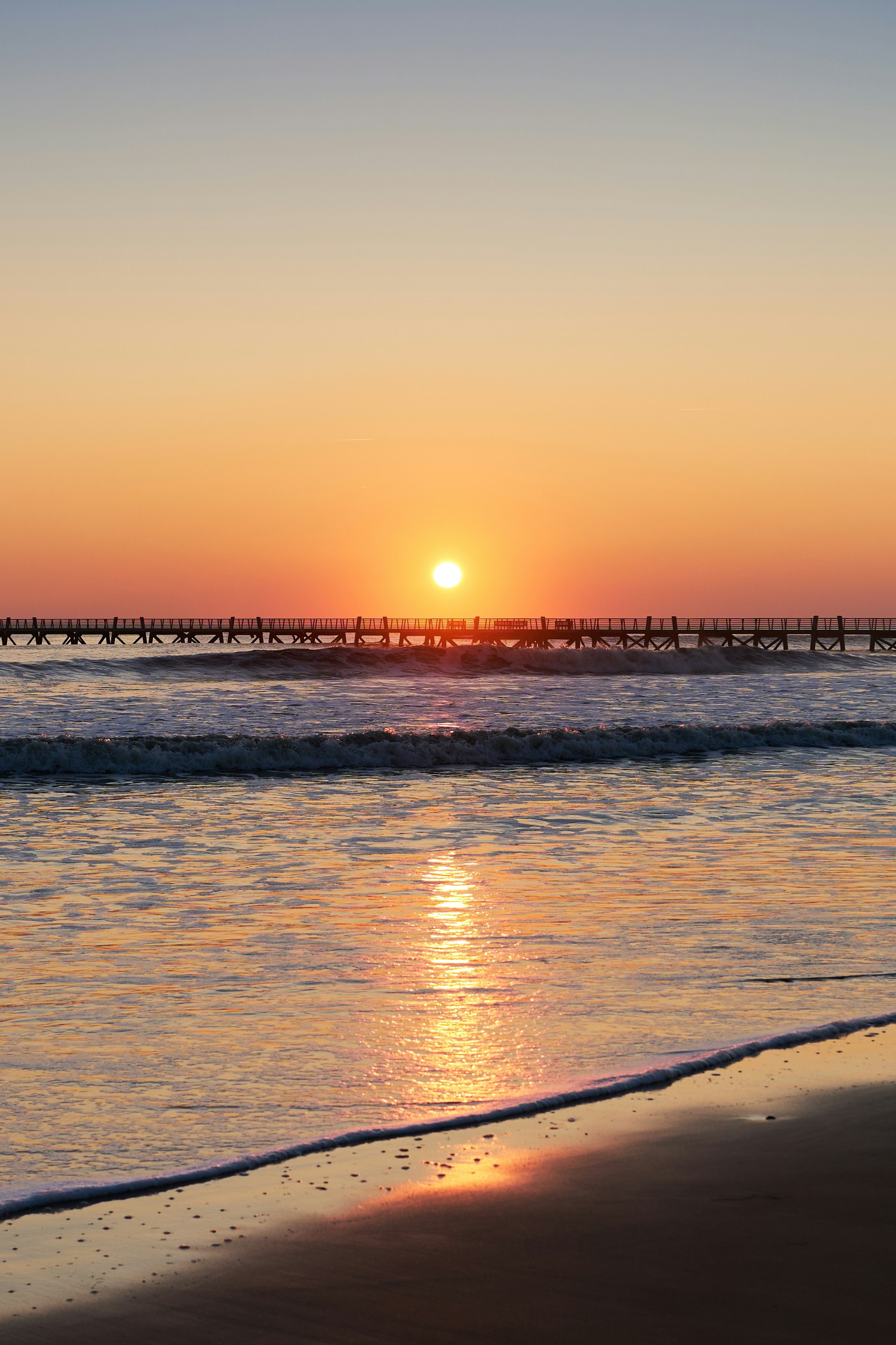 The sun is setting over the ocean with a pier in the distance