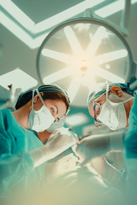 Two surgeons in masks and scrubs performing surgery under bright overhead lights