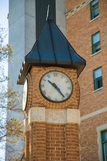 A brick clock tower stands against a brick building.