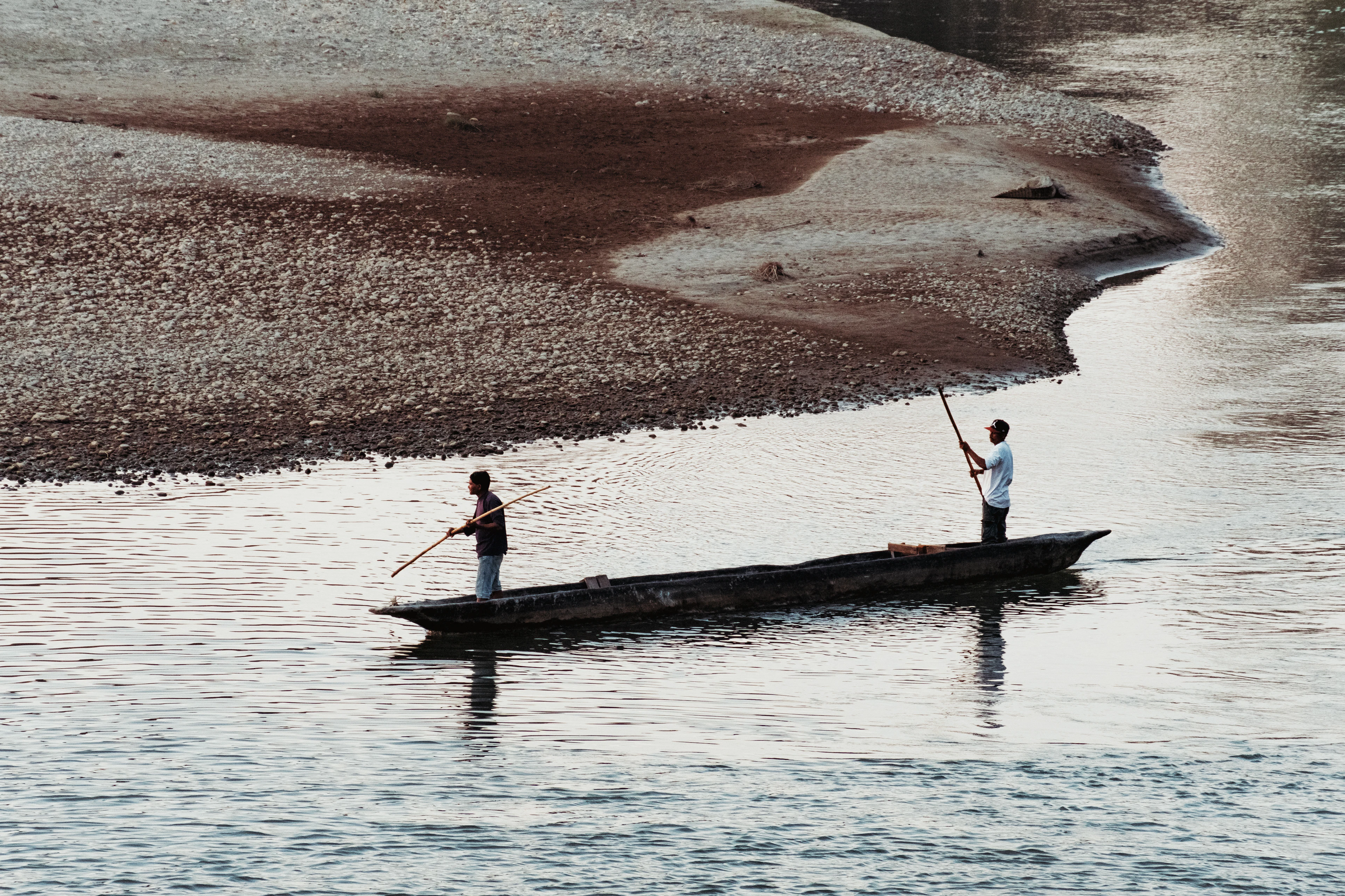 Two men poling a wooden canoe along a river in Chitwan National Park