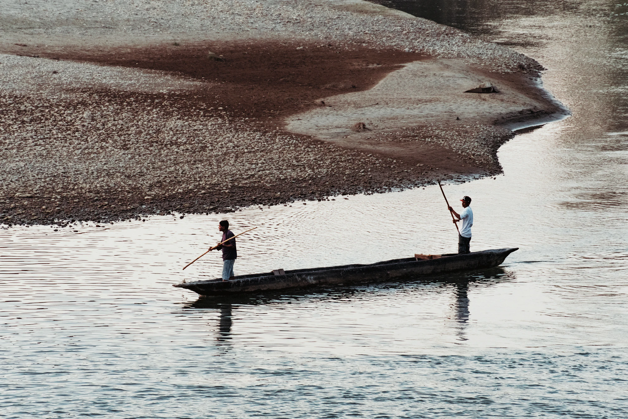 Two people in a wooden dugout canoe drifting along the Rapti River through the jungle in Chitwan, Nepal