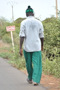 A man walks on a road past a sign.