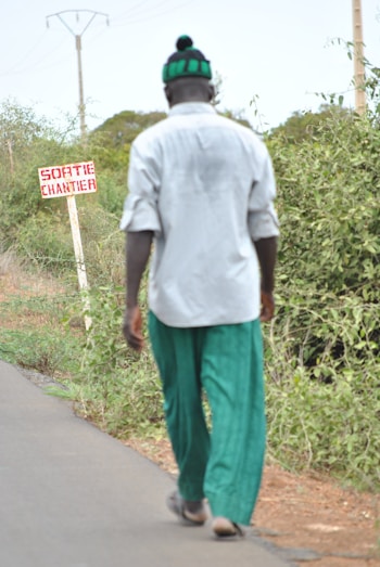 A man walks on a road past a sign.