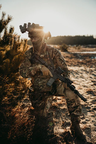 A soldier kneels in camouflage at sunset.