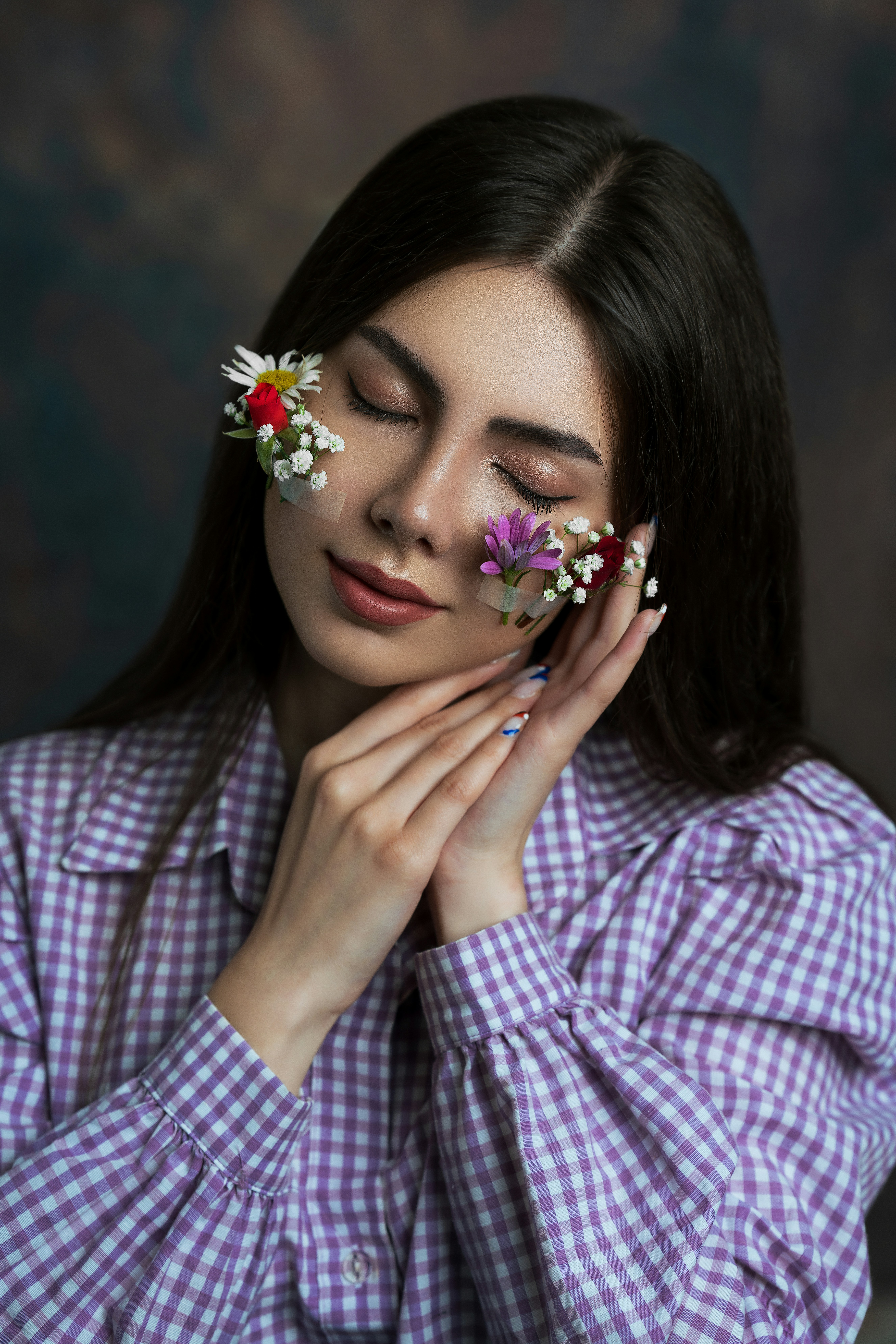 Woman gently poses with flowers on her face.