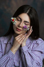 Woman gently poses with flowers on her face.