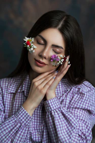 Woman gently poses with flowers on her face.