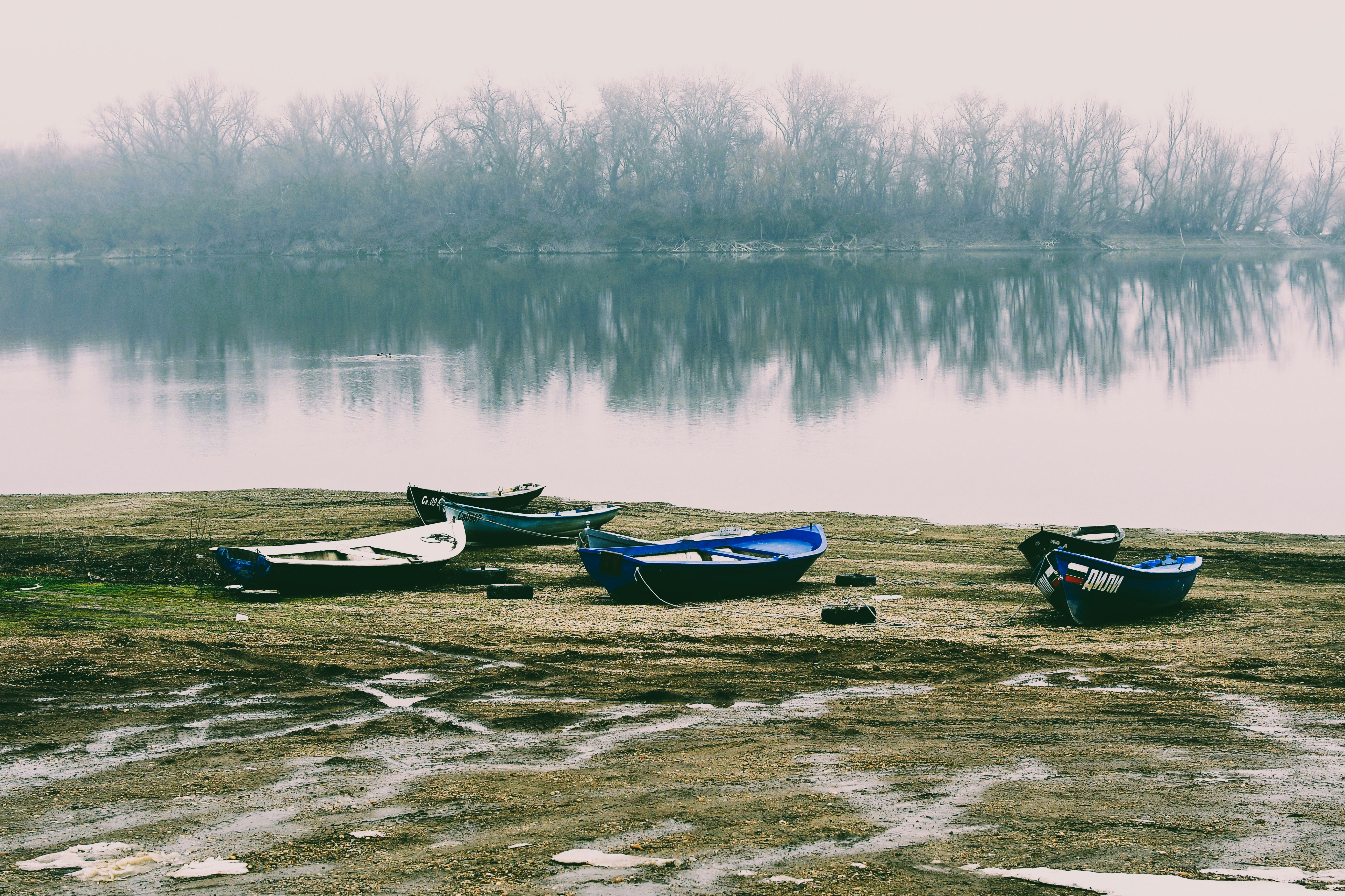 Boats sit on the shore of a misty lake.