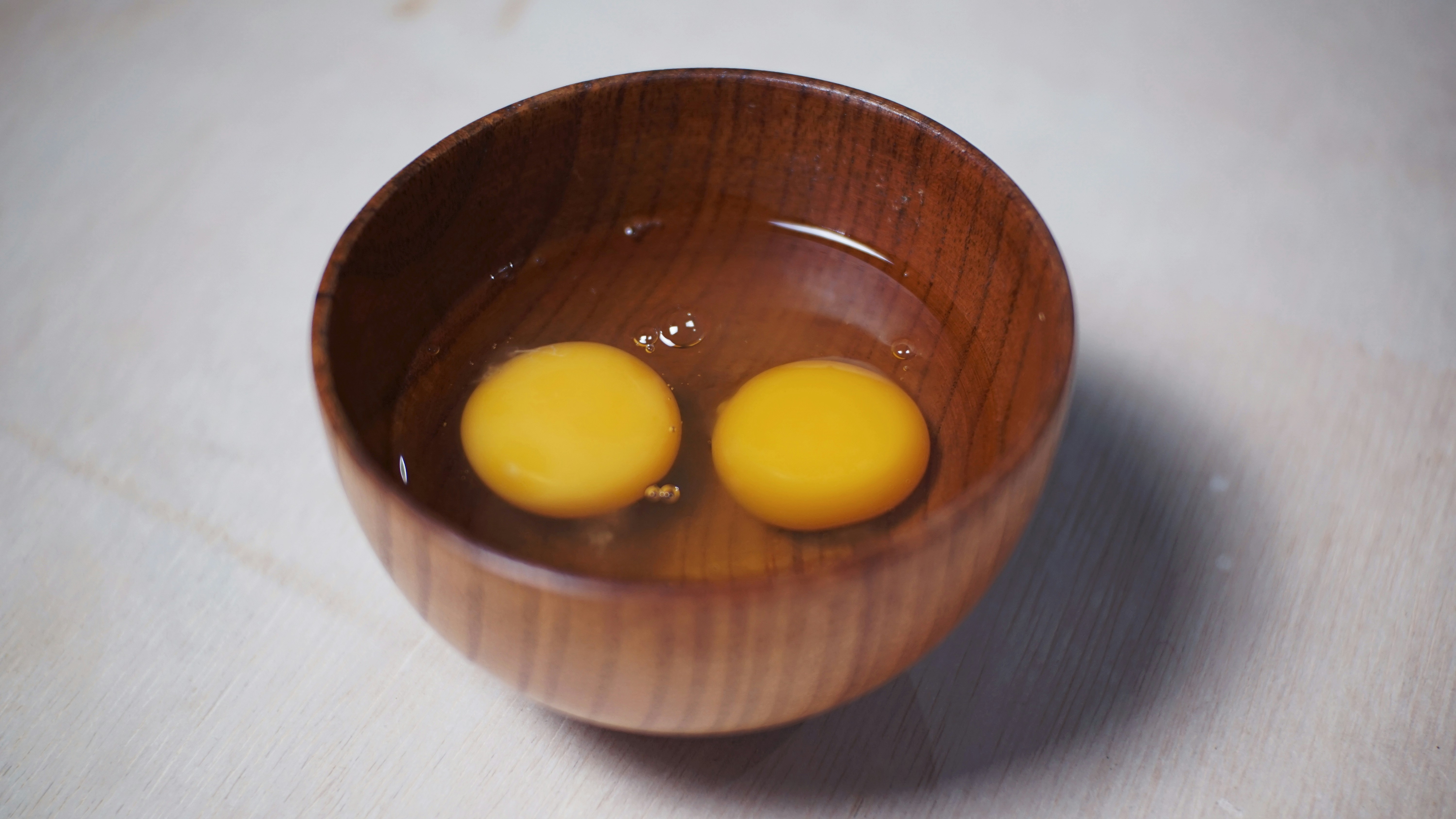 Two raw egg yolks sit in a wooden bowl.