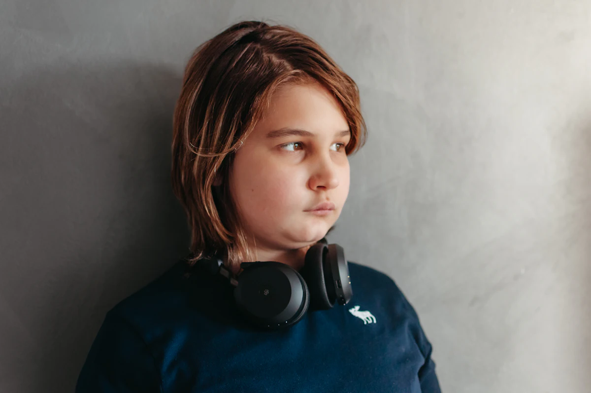 A boy wearing over-ear headphones, looking calmly to one side.