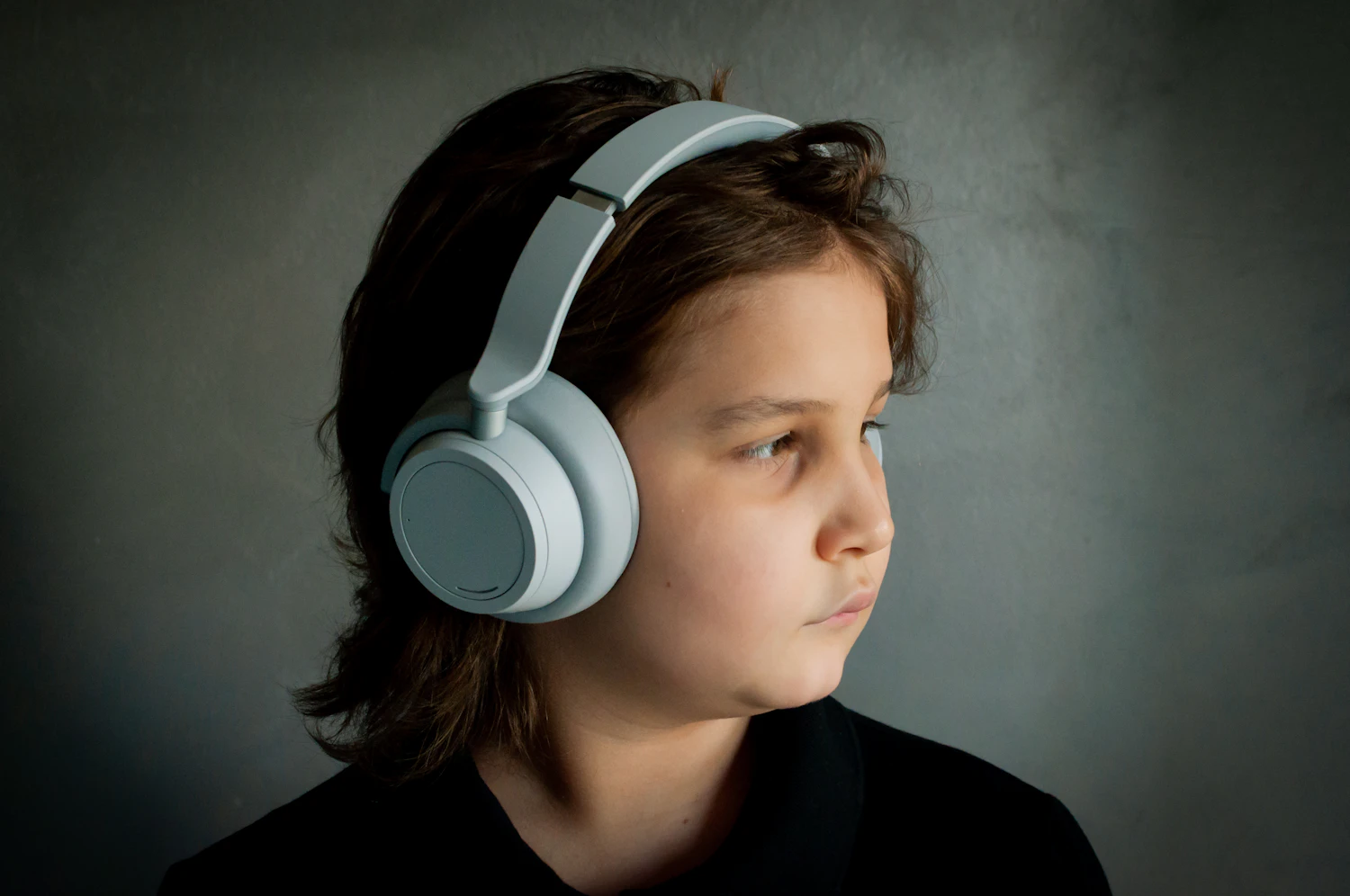 A child wearing light gray over-ear headphones, looking off to the side