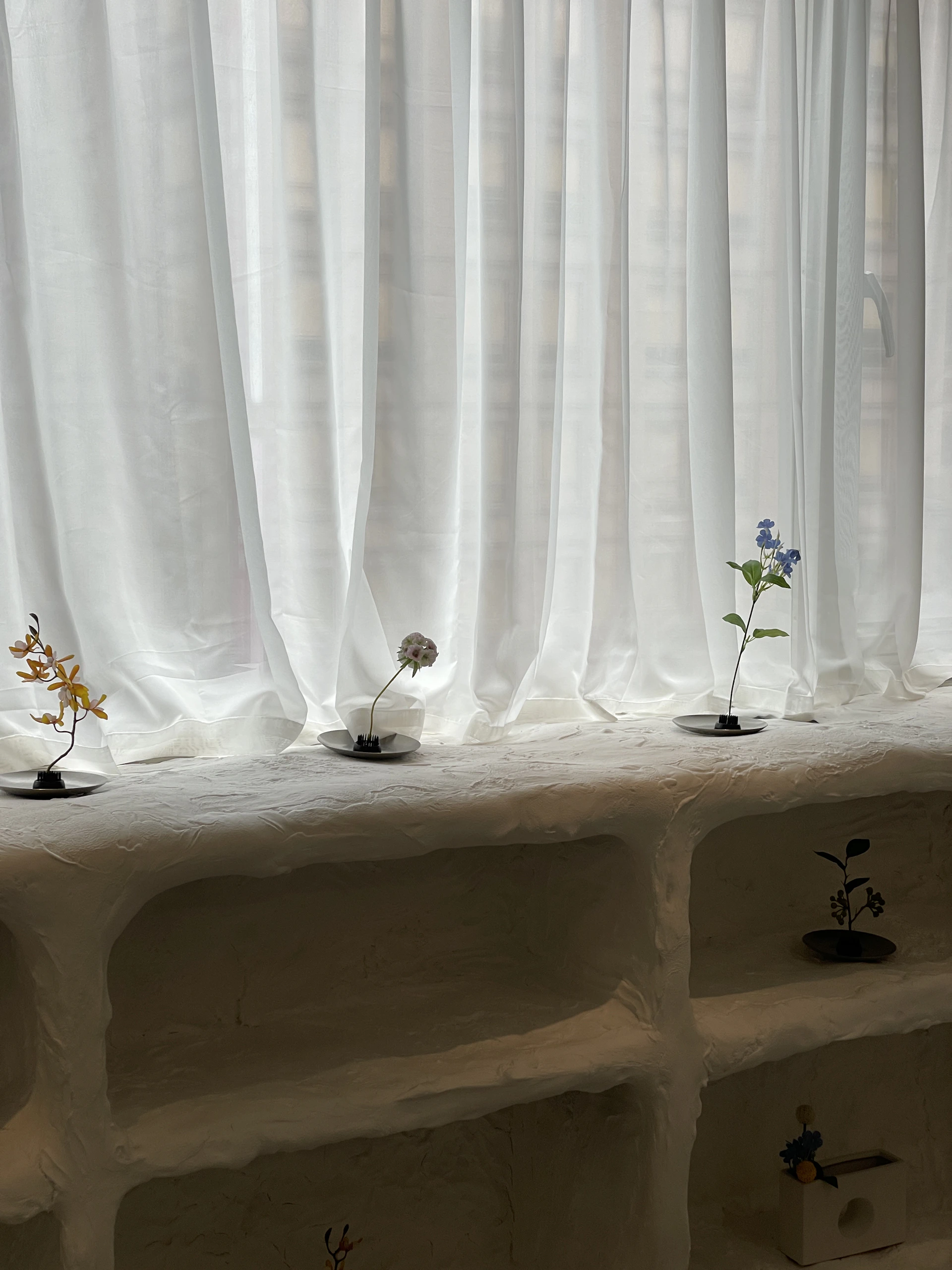 Flowers are placed on a windowsill with white curtains.