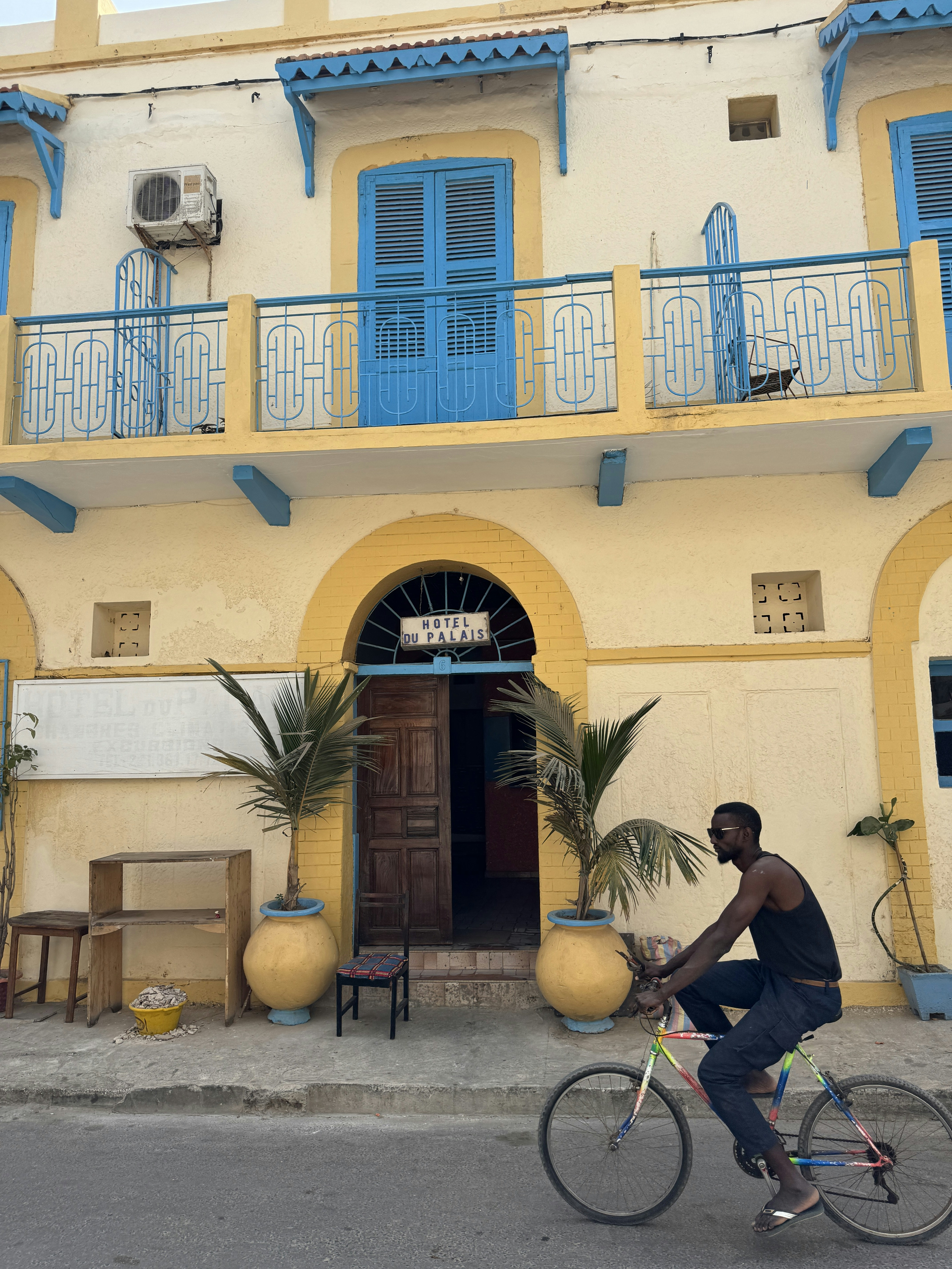 黄色と青の建物を自転車で通り過ぎる男性