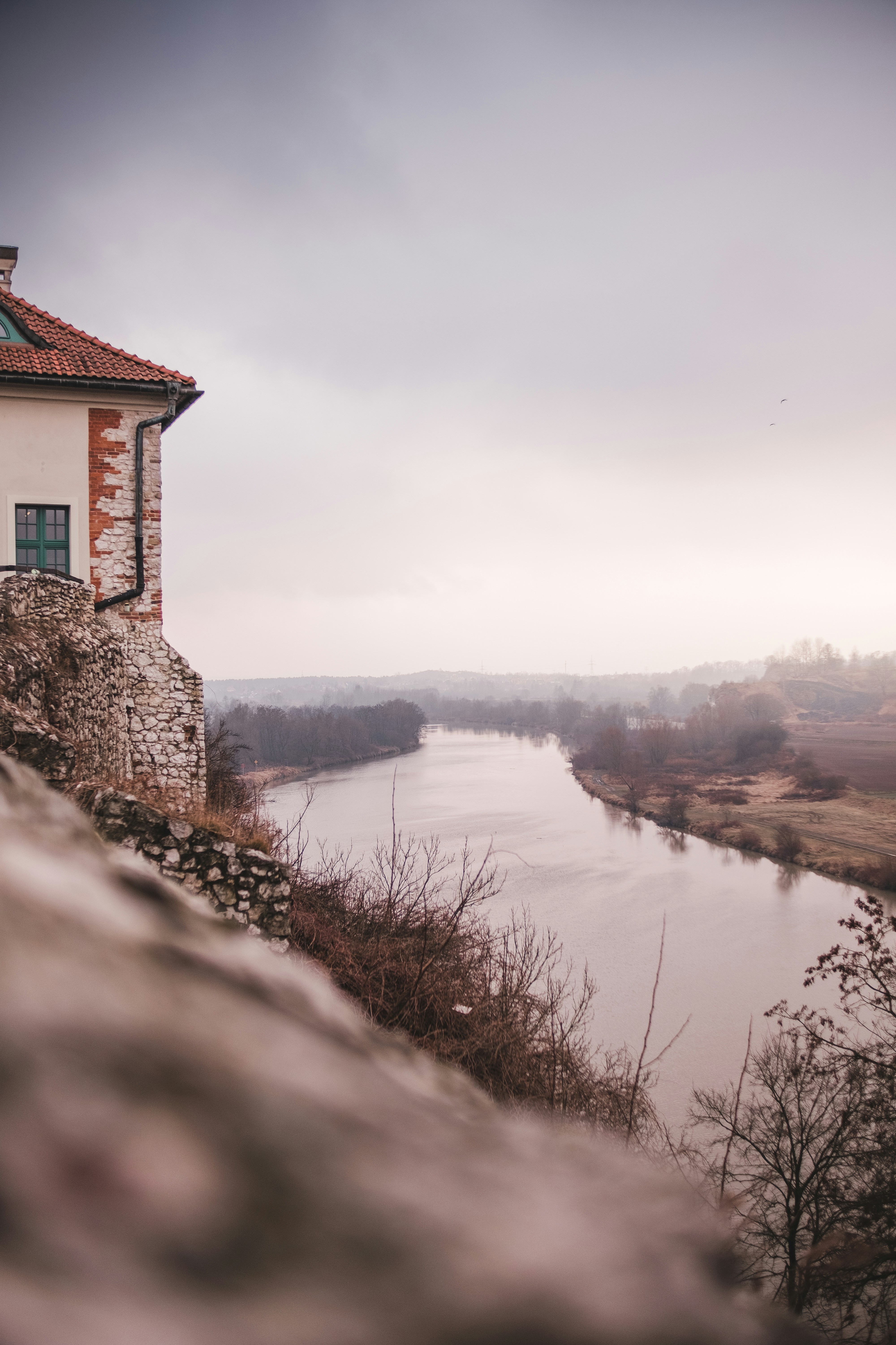 A castle overlooks a river on a cloudy day.