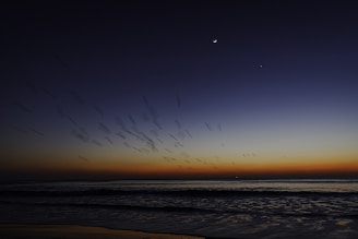 Sunrise over the ocean with planets above.