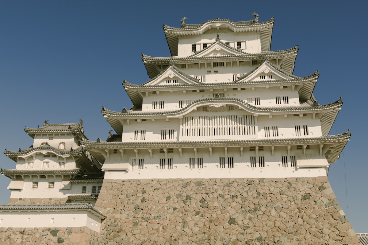 Japanese castle tower rising above ancient stone walls, surrounded by autumn foliage