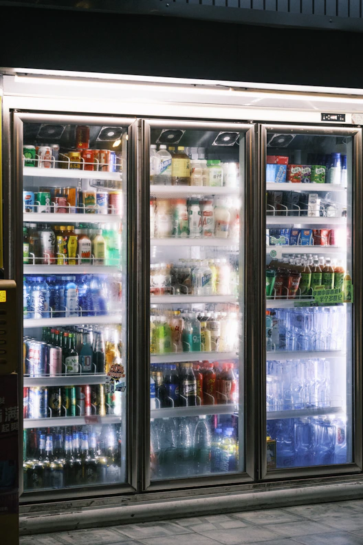 Three illuminated refrigerators full of beverages.