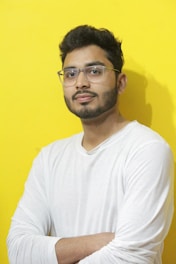 A man is posing in front of a yellow wall.