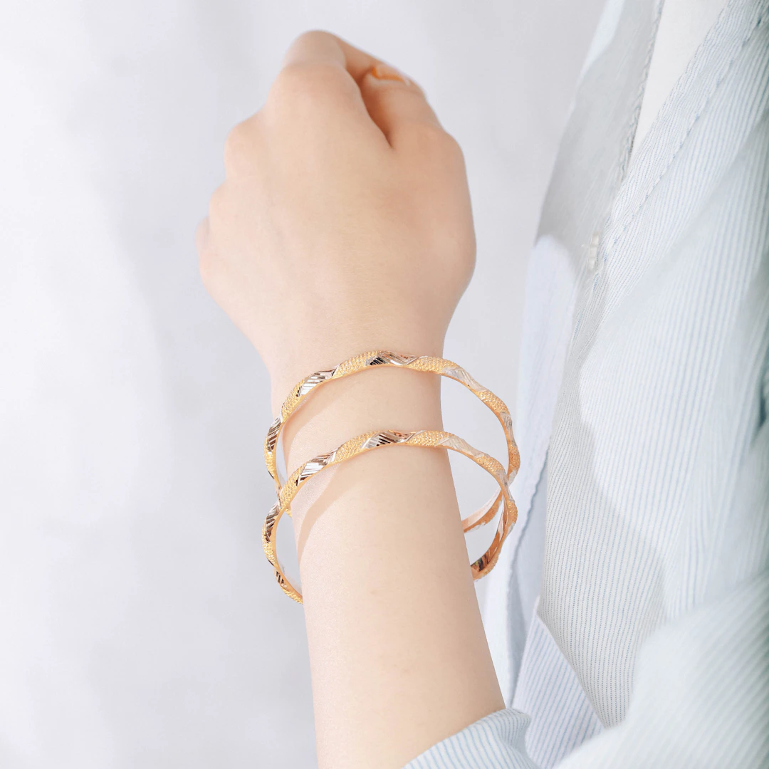Braço feminino com duas pulseiras de elos dourados.