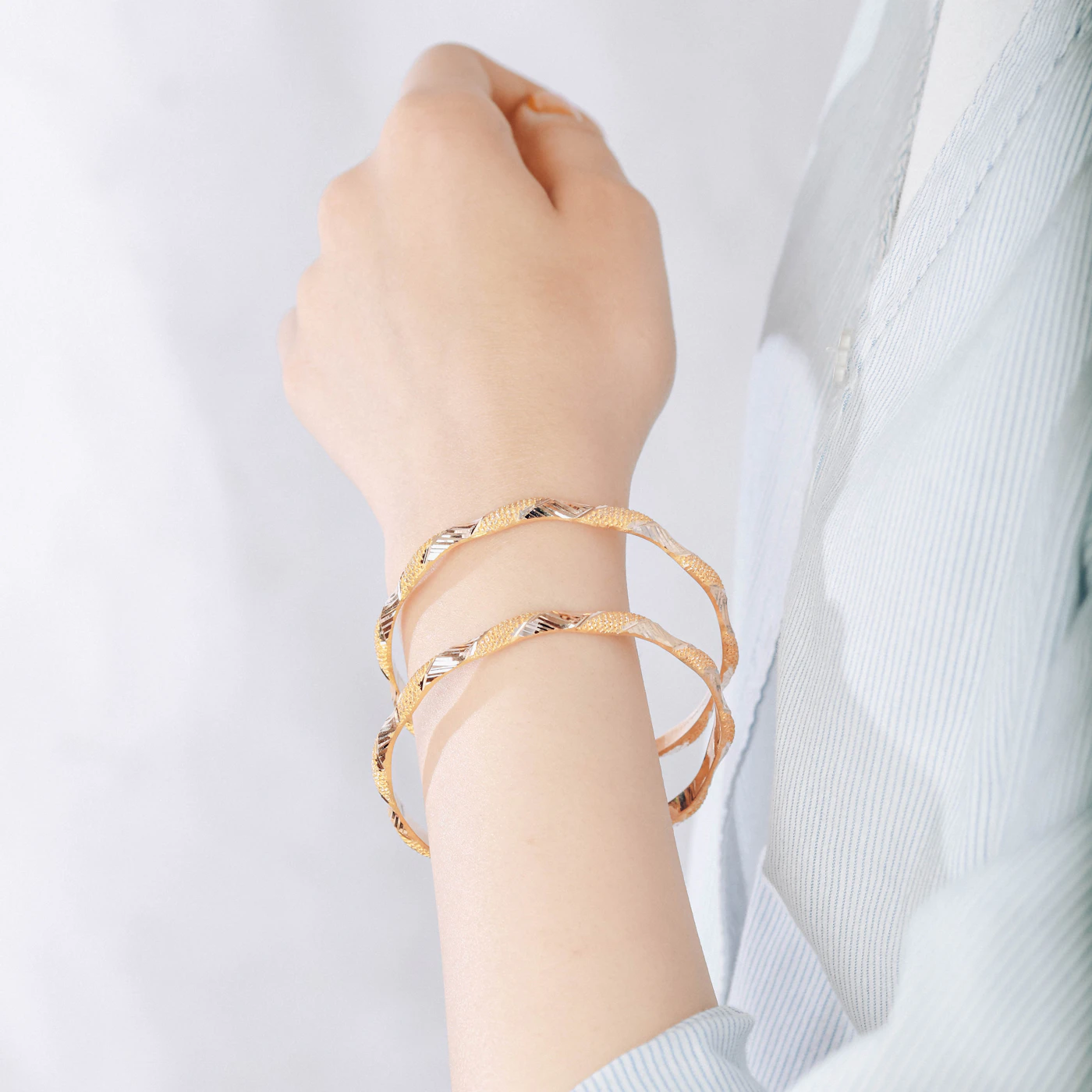 Two gold bracelets on a woman's wrist
