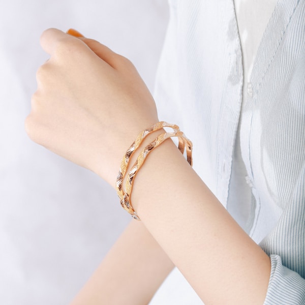A person wears gold bracelets on wrist.