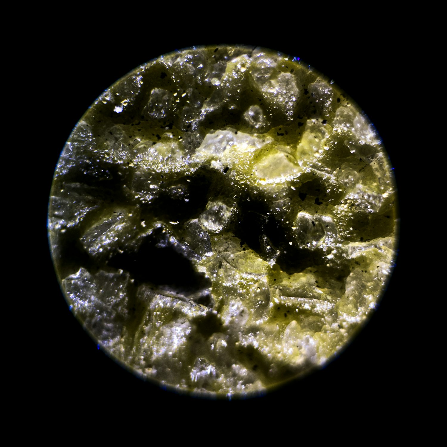 A microscopic close-up of a sheet of sandpaper. You can see individual yellow grains of sand caught by the light. Some grains are semi-translucent.