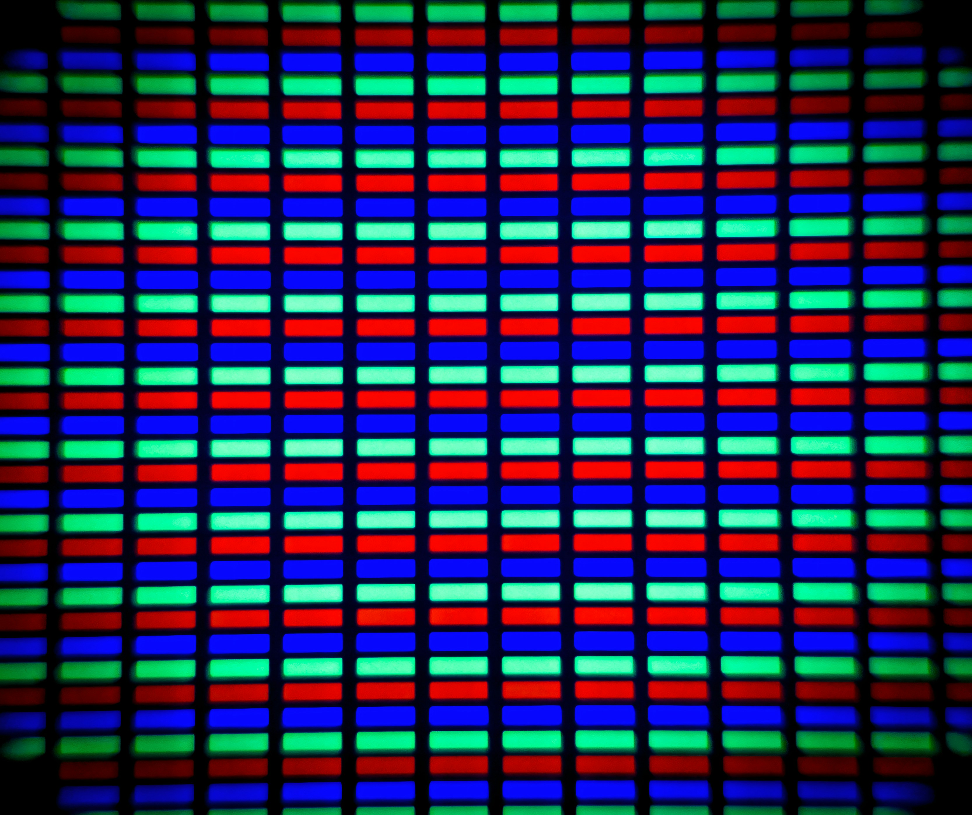 A microscopic close-up of an LCD screen. You can see individual red, green, and blue subpixels in a grid. The edges of the photo are darkened and slightly blurred.