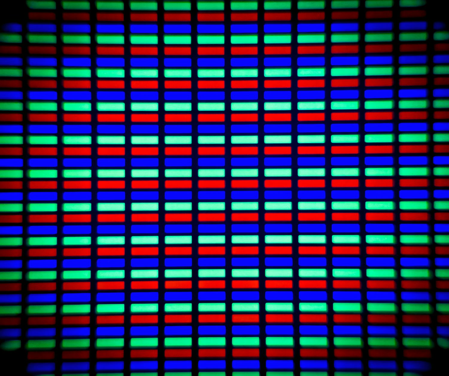 A microscopic close-up of an LCD screen. You can see individual red, green, and blue subpixels in a grid. The edges of the photo are darkened and slightly blurred.