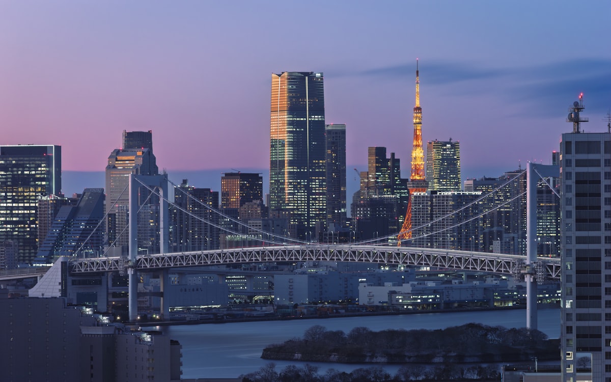 The Tokyo skyline and Rainbow Bridge illuminated at dusk with city lights reflecting on the water