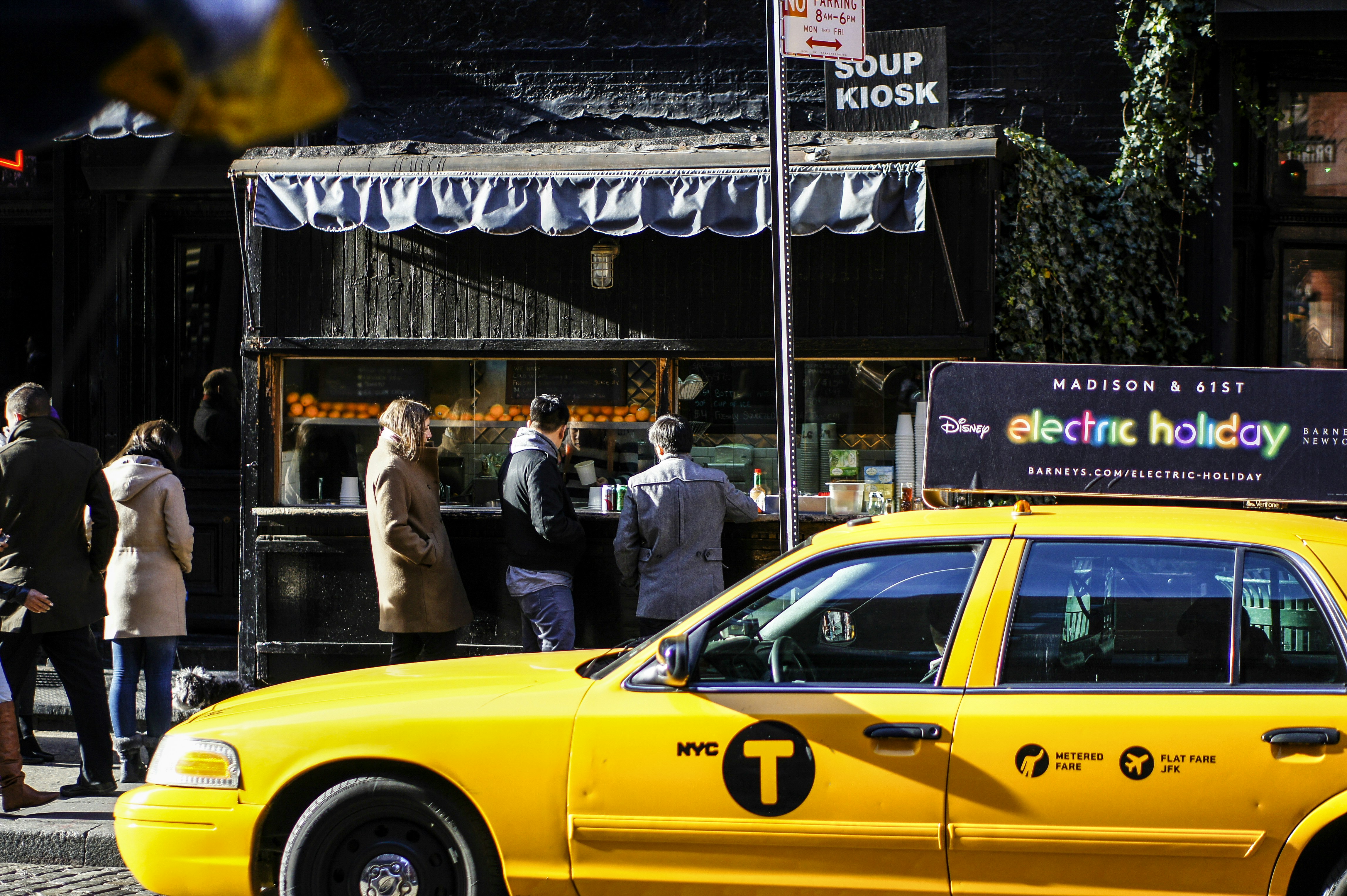 A yellow taxi sits in front of a new york soup kiosk.