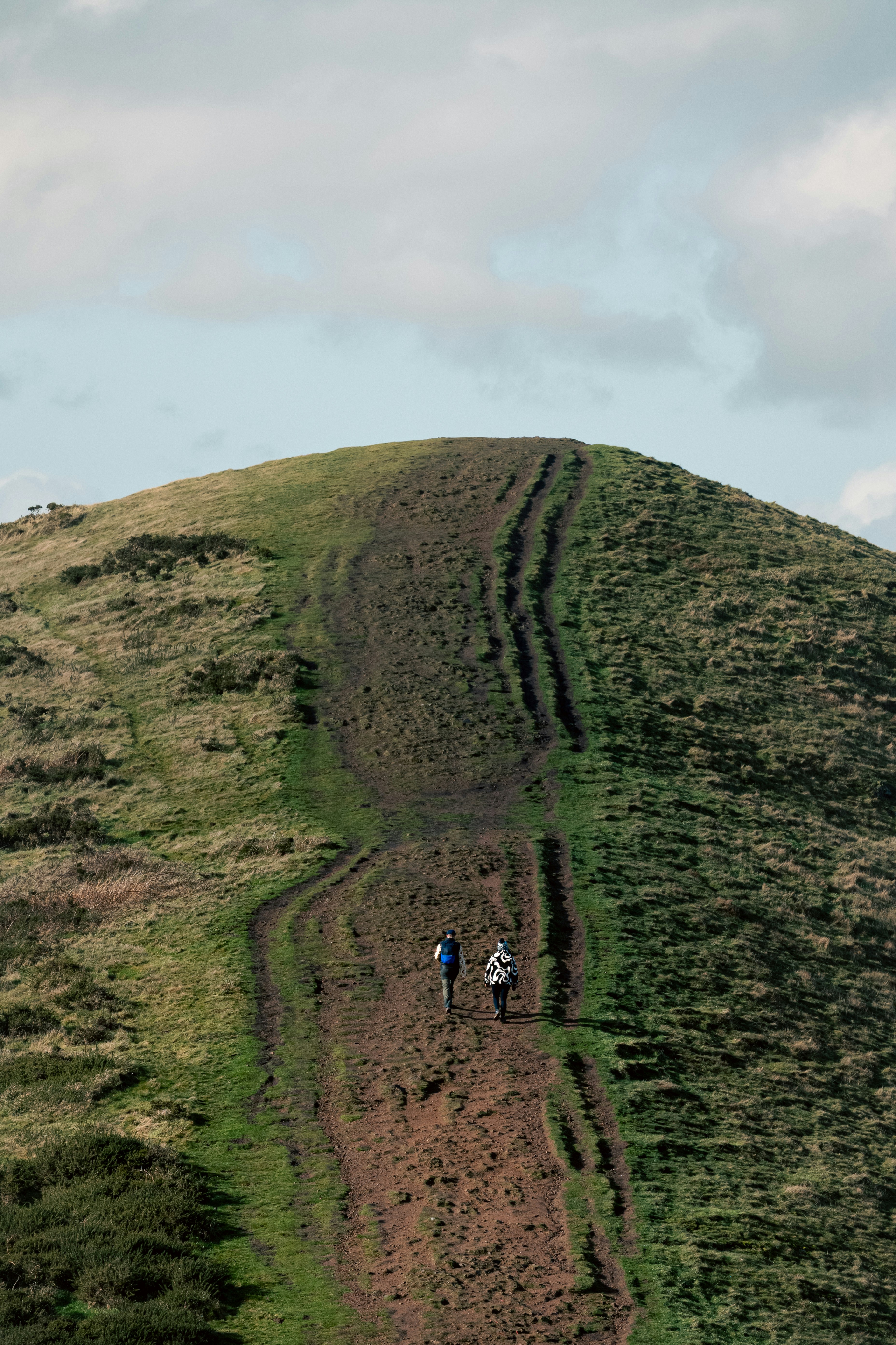 Duas pessoas sobem uma colina gramada.