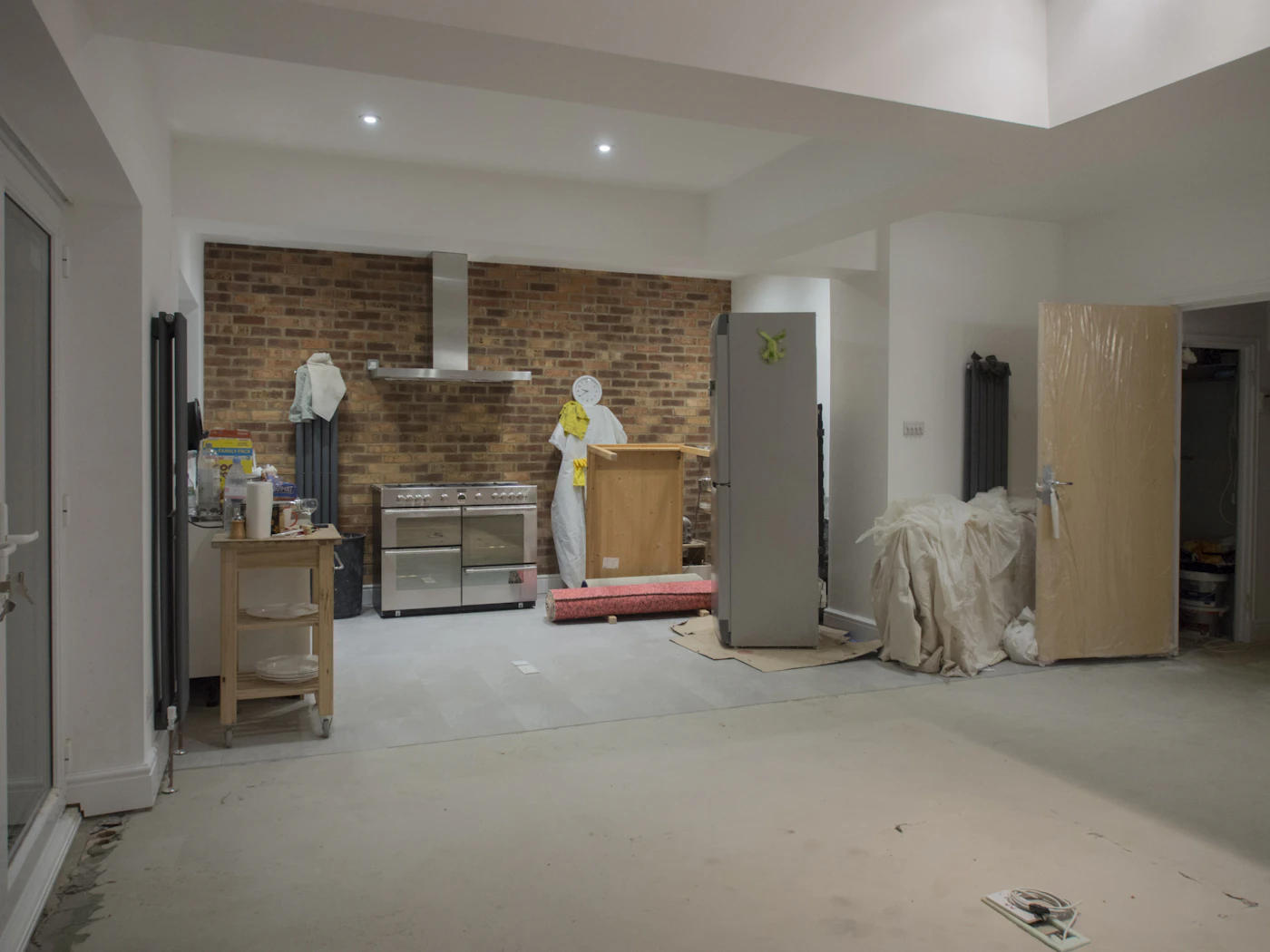 Kitchen during remodel with exposed brick wall and staged appliances