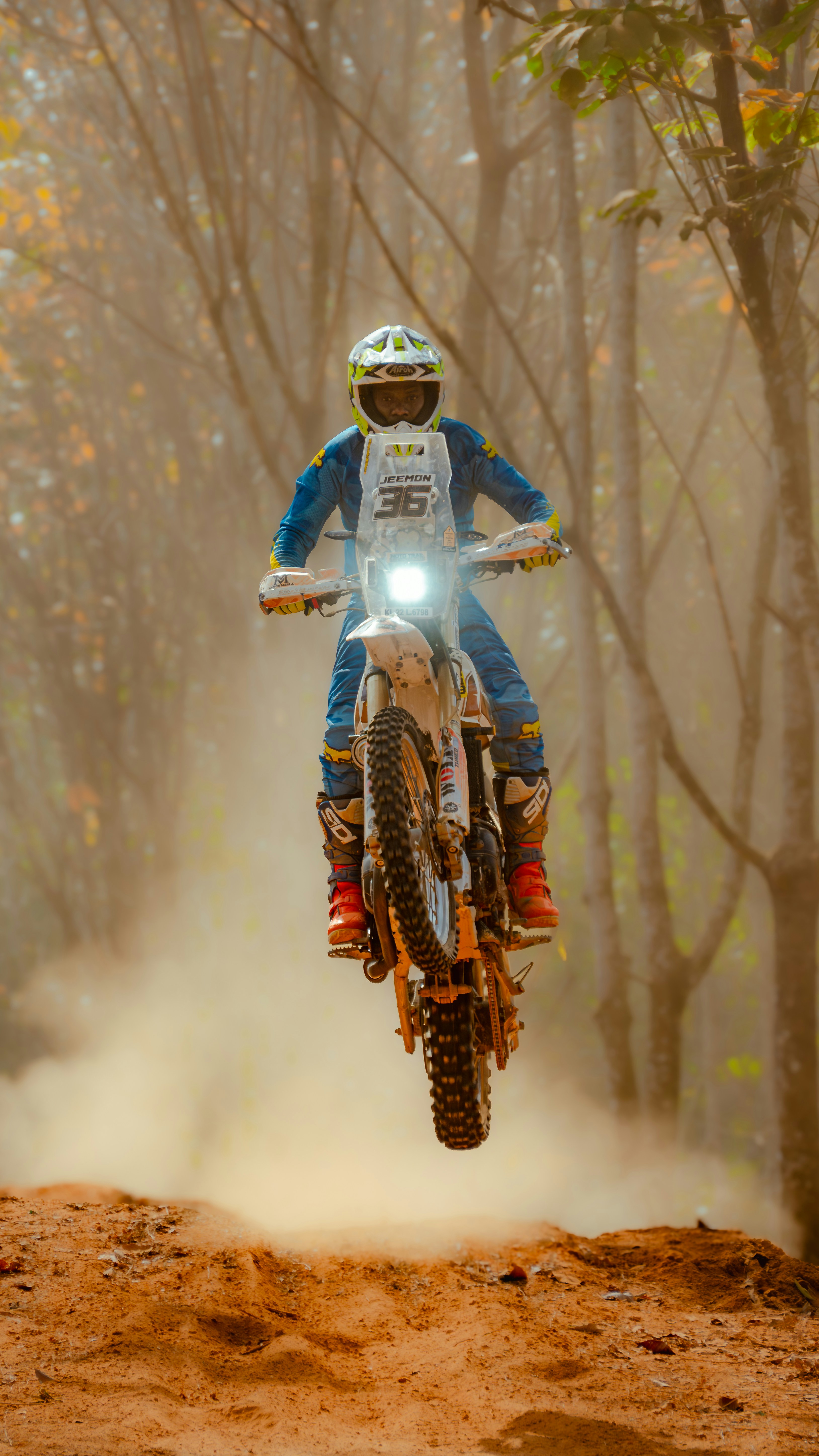Un motocycliste saute haut sur un chemin de terre poussiéreux.
