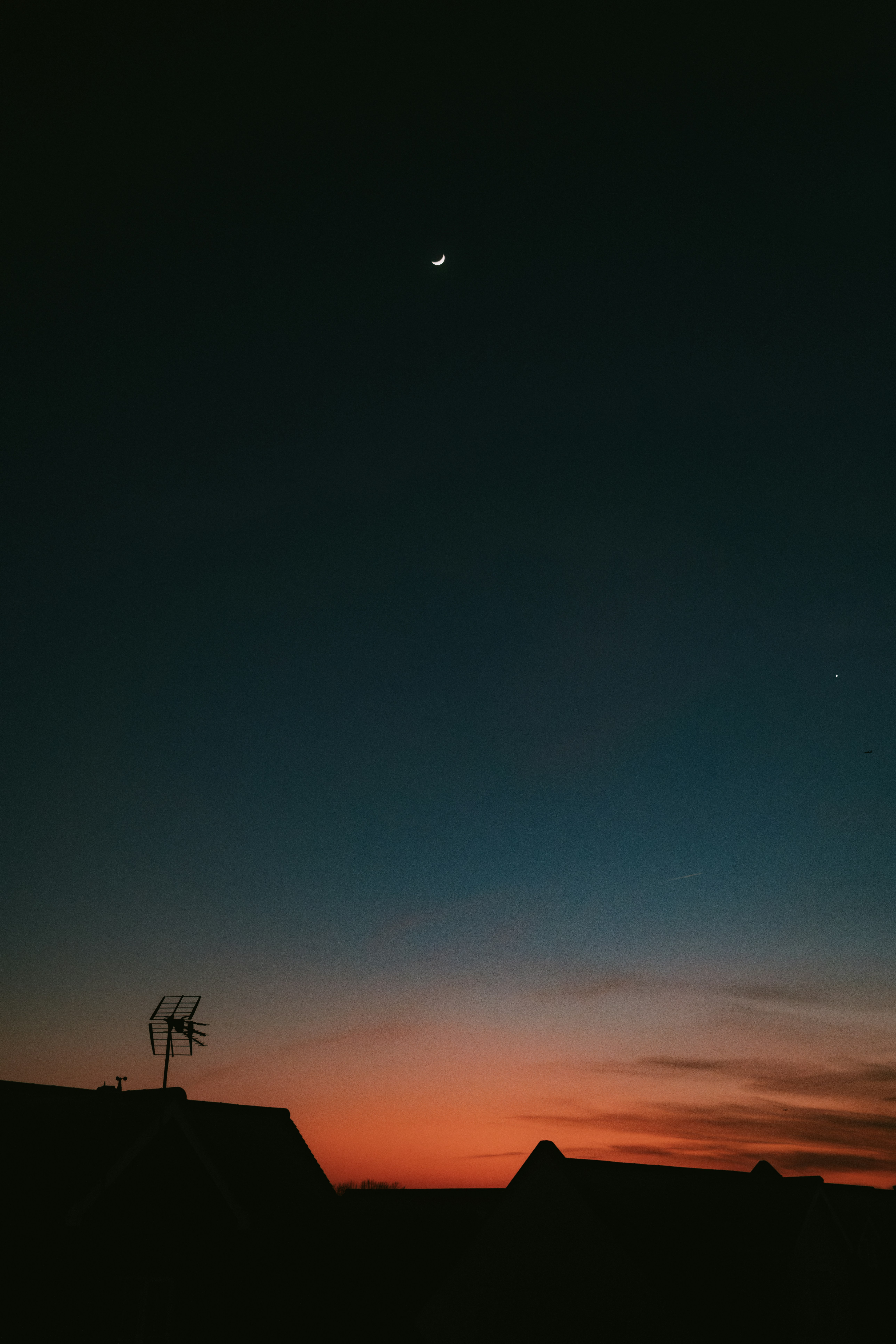 Sunset sky with moon and silhouette rooftop.