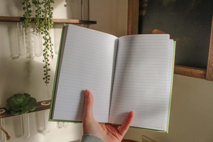 Hands holding an open notebook over a desk, reviewing monthly notes near a small office plant
