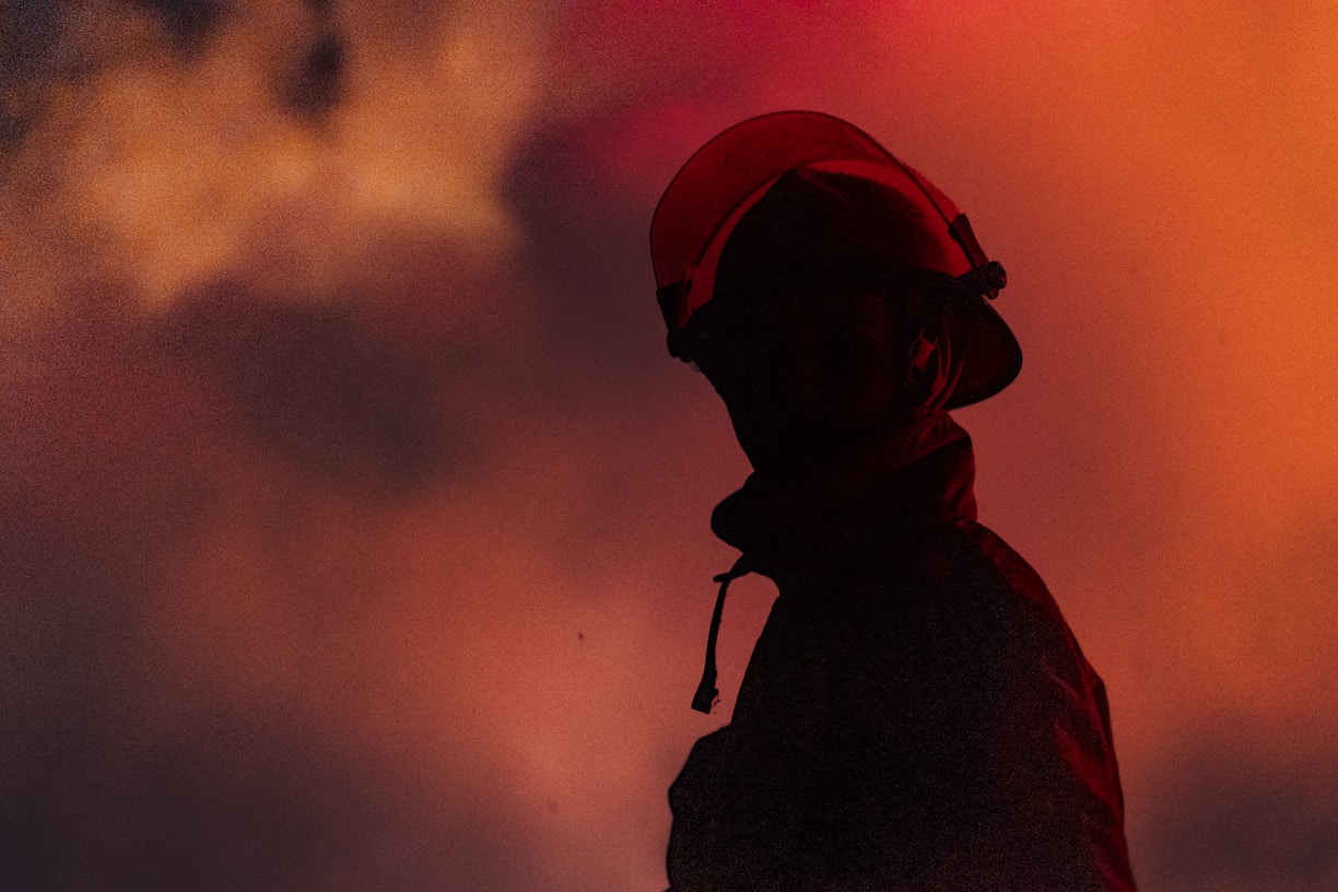 A firefighter stands in front of a fiery sky.