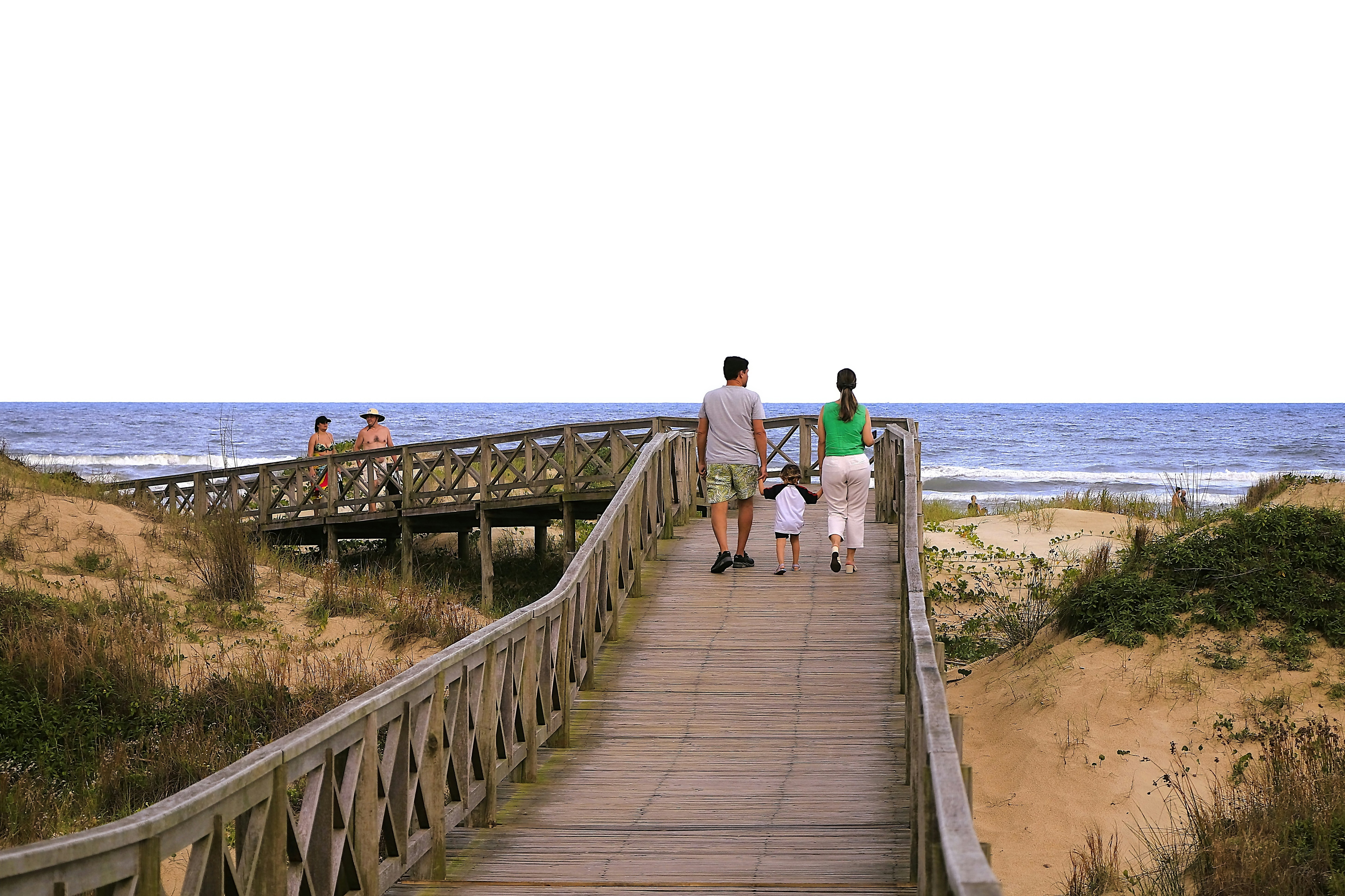 Família passeia em um calçadão em direção à praia.