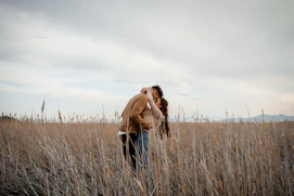 Couple shares a kiss in a field.