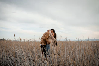 Couple shares a kiss in a field.