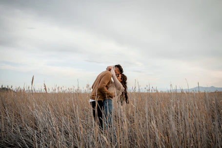 Couple shares a kiss in a field.