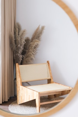 Mirror reflects a chair, pampas grass, and curtains.