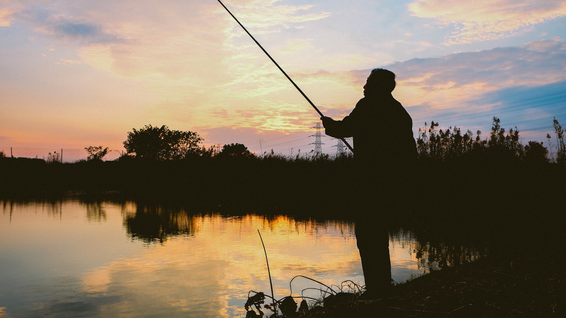 A person fishes at sunset over calm water.