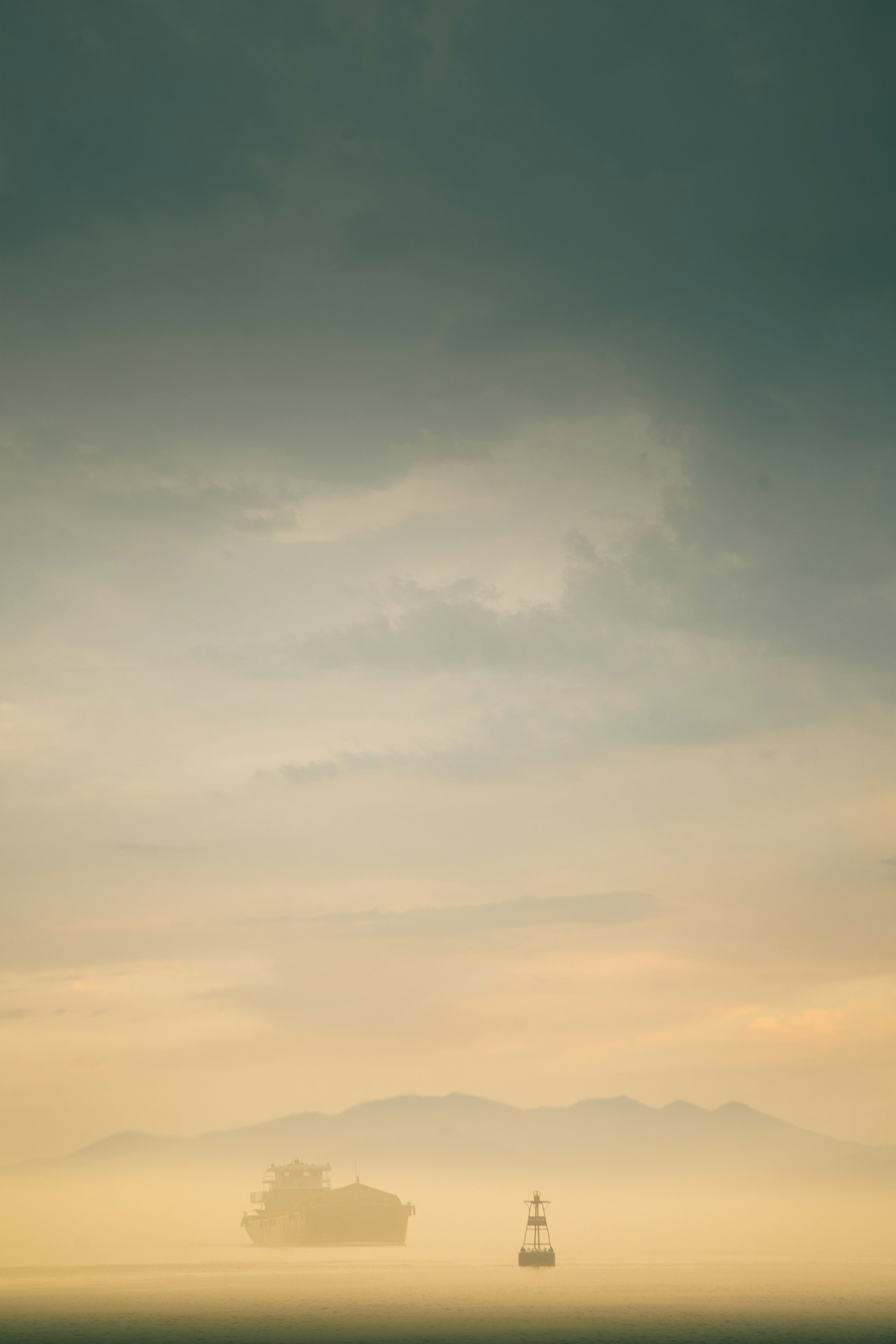 Foggy landscape with a distant boat and mountains.